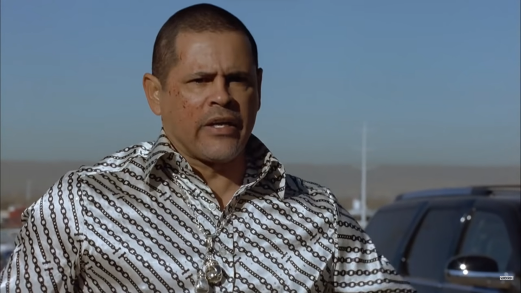 Tuco Salamanca in a silk white shirt standing near the black car in the background