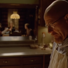 Walter White in a white t-shirt and glasses, woman at the table behind on blurred background