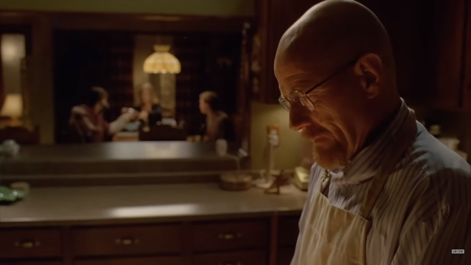 Walter White in a white t-shirt and glasses, woman at the table behind on blurred background