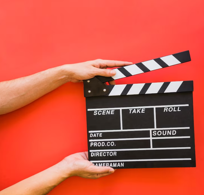 hands holding a clapperboard with words scene, take, roll on it in front of a red background