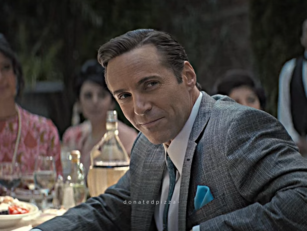 dicky montesanti in a gray classic suit sitting at the table, women behind him on blurred background