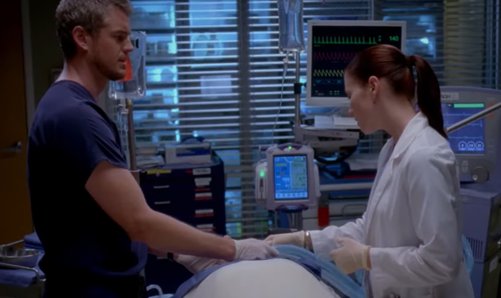 Mark and Lexie in grey anatomy stand near the body’s patient and hold hands